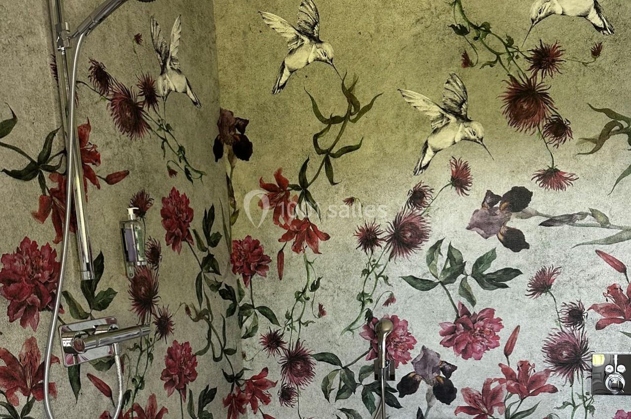 Douche avec robinetterie chromée, mur décoré de motifs floraux rouges et d'oiseaux sur fond vert.
