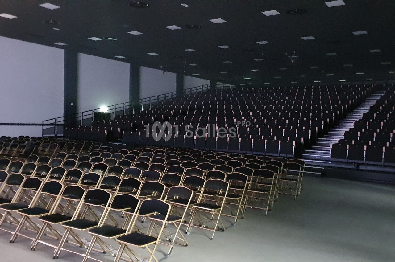 Salle de conférence vide avec des rangées de chaises pliantes et des gradins en arrière-plan.