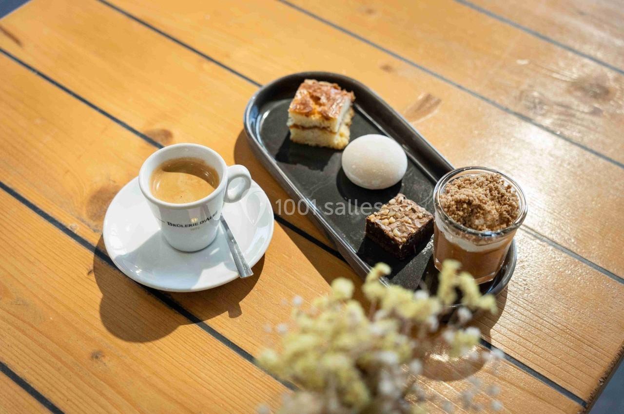 Tasse de café avec un plateau contenant des desserts variés sur une table en bois clair.