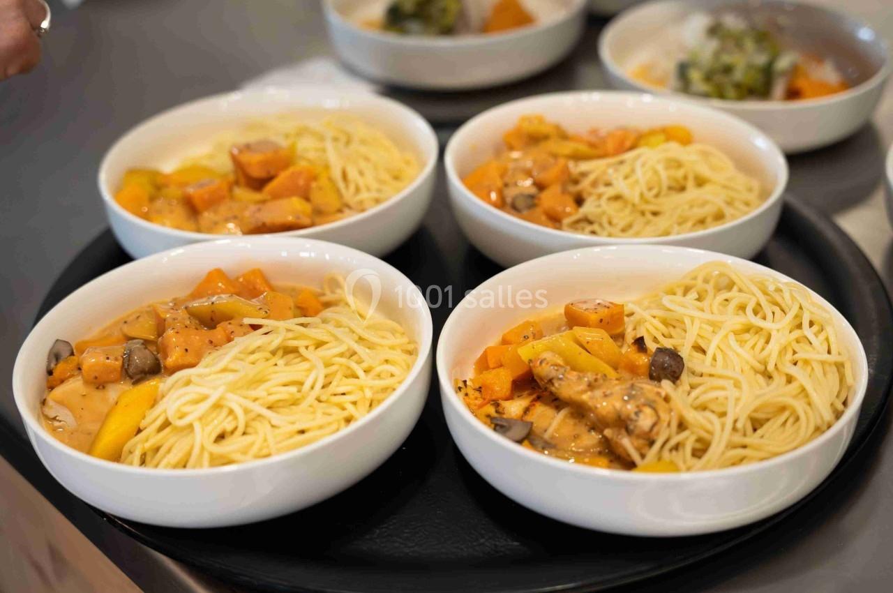 Quatre assiettes de spaghettis accompagnés de légumes et d'une sauce crémeuse, servies sur un plateau noir.