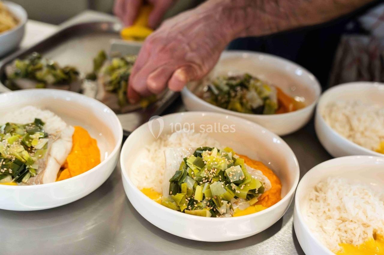 Une main sert des plats composés de riz, légumes verts, purée orange et poisson dans des bols blancs.