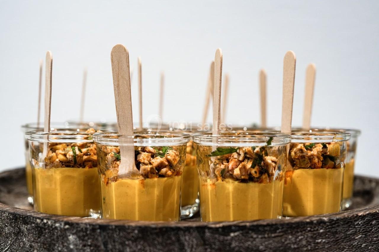 Verrines de soupe jaune garnies de morceaux de poulet et de persil, avec des bâtonnets en bois pour servir.