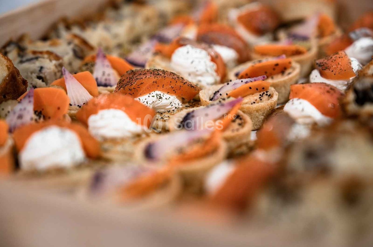 Assortiment de canapés garnis de saumon fumé, crème fraîche et herbes, disposés sur un plateau.