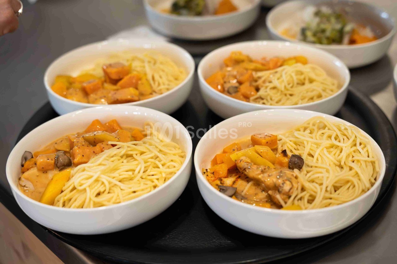 Quatre assiettes de spaghettis accompagnées de légumes en sauce servies sur un plateau noir.