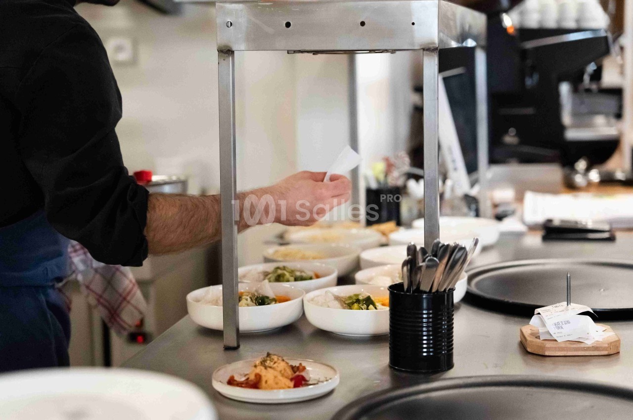 Un cuisinier prépare des plats dans une cuisine professionnelle, avec des bols alignés sur un plan de travail.
