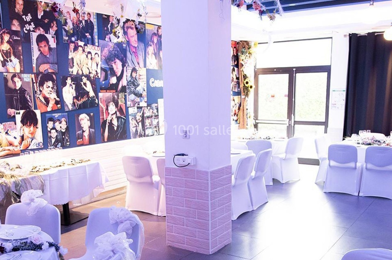 Salle décorée avec des affiches de musiciens, tables dressées avec nappes blanches et chaises recouvertes.