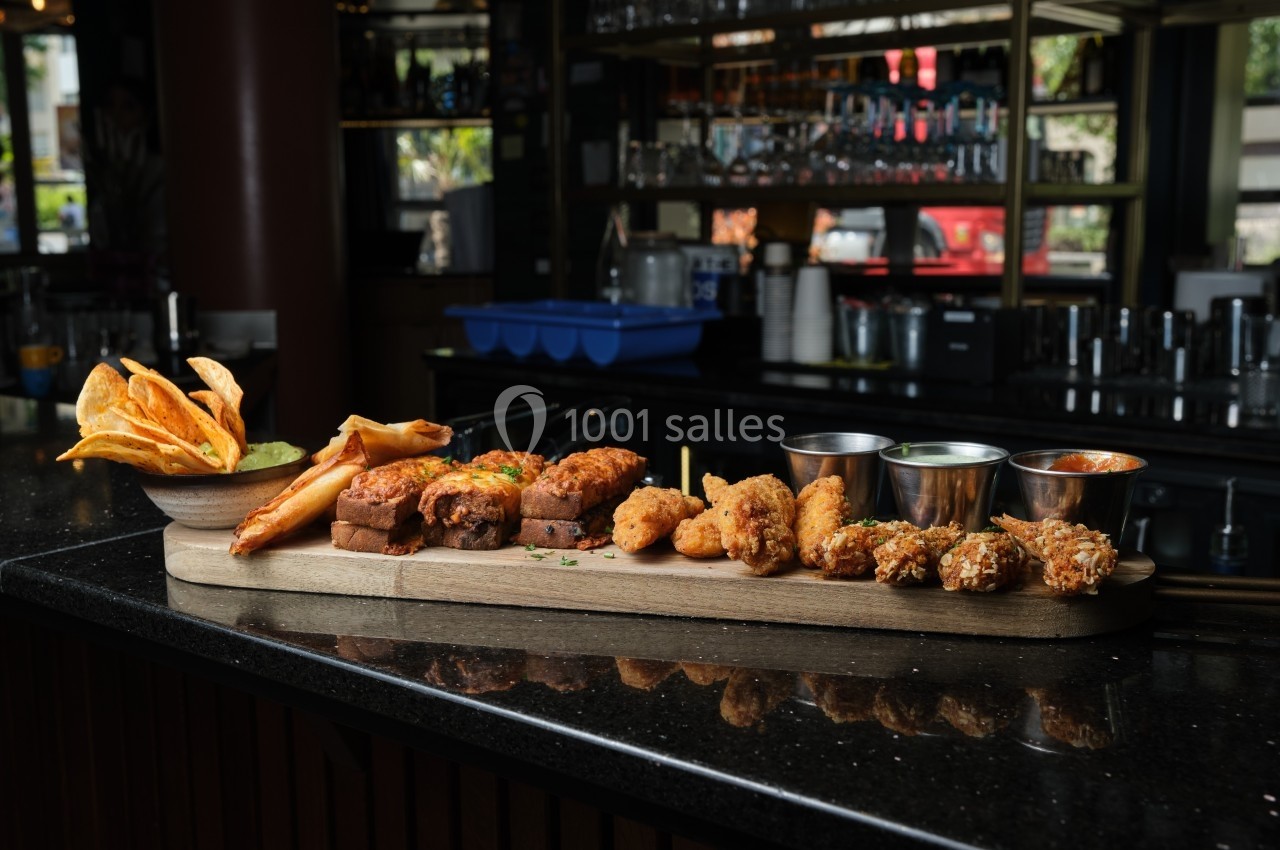 Plateau de tapas variés avec sauces, frites de patate douce et snacks frits, posé sur un comptoir de bar sombre.