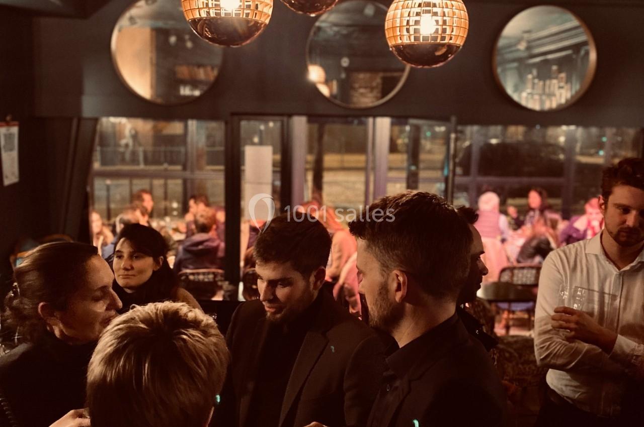 Groupe de personnes discutant dans un bar à l'ambiance tamisée, éclairé par des suspensions lumineuses.