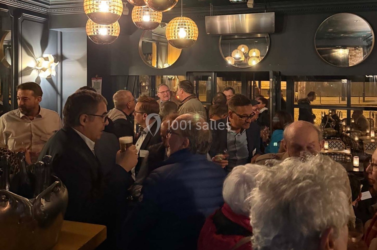 Groupe de personnes discutant et partageant des boissons dans un bar à l'ambiance tamisée et chaleureuse.