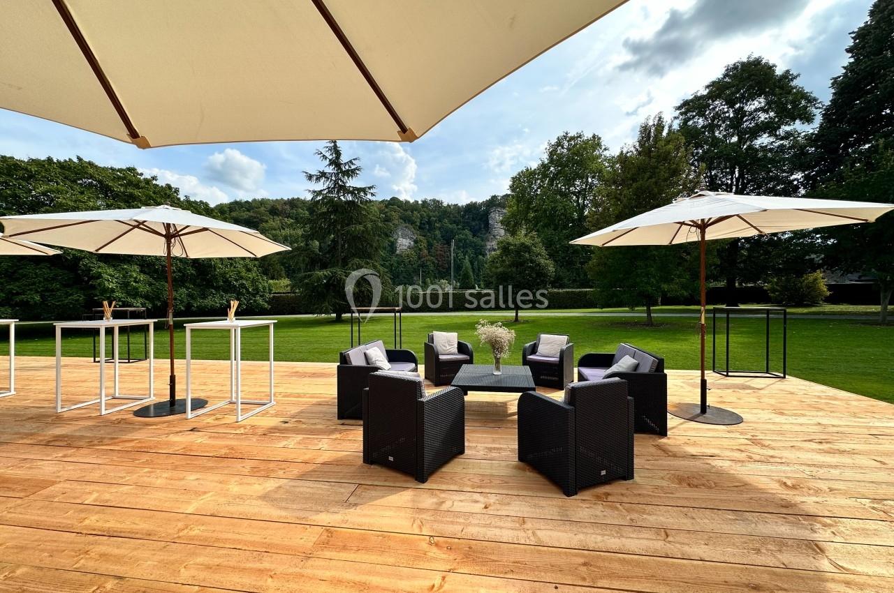 Terrasse en bois avec mobilier de jardin noir, parasols blancs et vue sur un parc verdoyant.