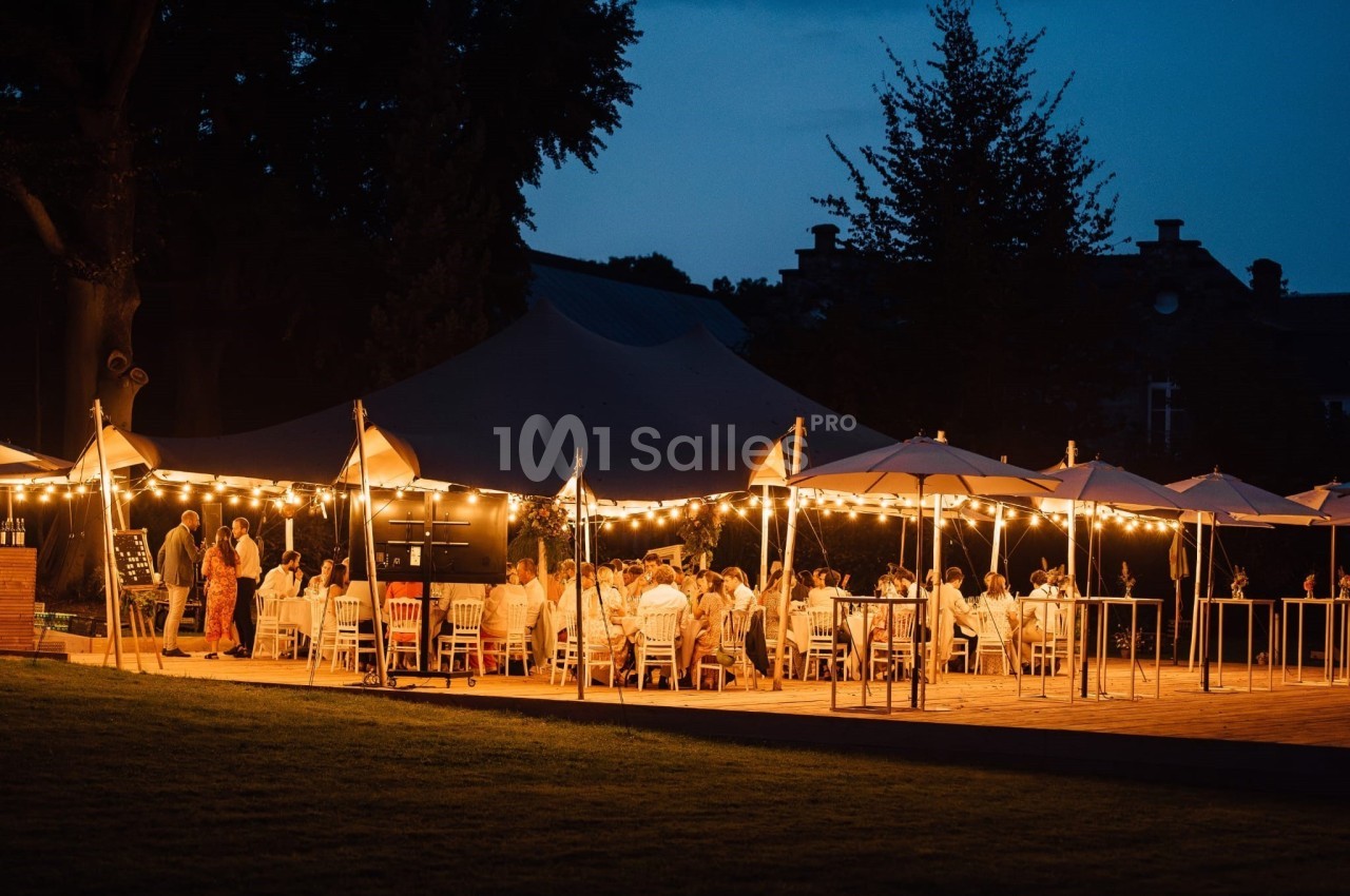 Dîner en plein air sous des guirlandes lumineuses, avec des invités assis autour de tables éclairées au crépuscule.