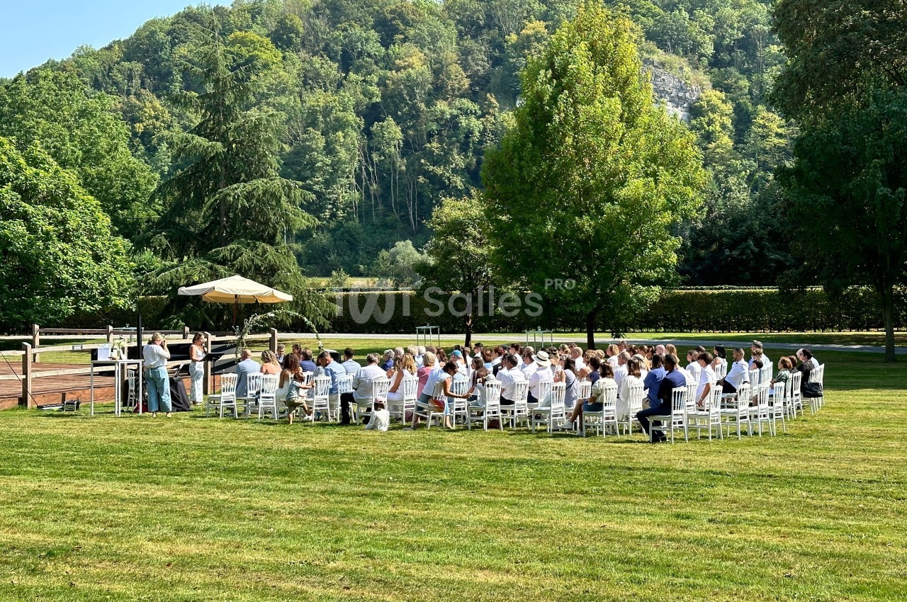 Cérémonie en plein air avec des invités assis en cercle sur une pelouse, entourée d'arbres et de collines verdoyantes.