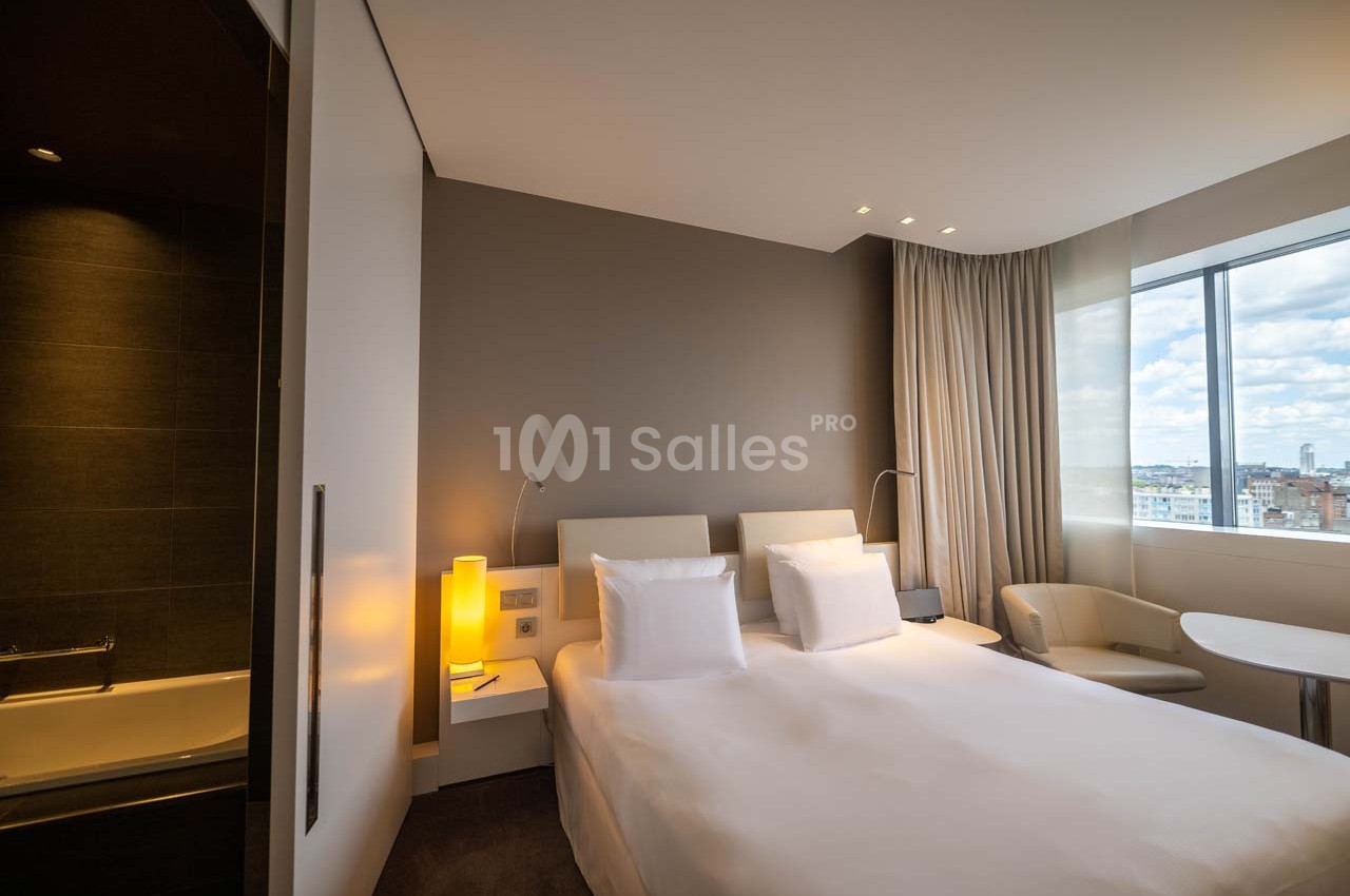 Chambre d'hôtel moderne avec lit double, éclairage doux, grande fenêtre et vue sur la ville.