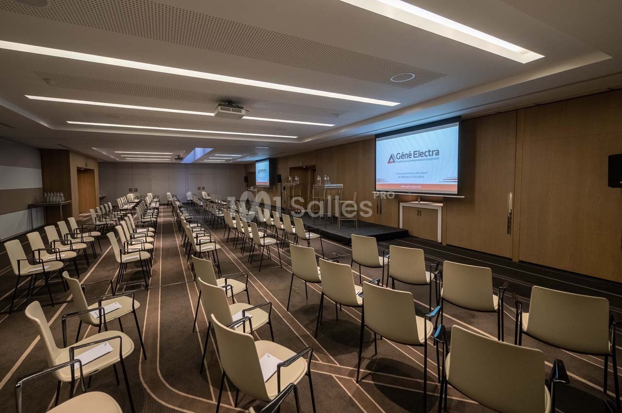 Salle de conférence moderne avec chaises alignées, écran de projection allumé et éclairage tamisé.