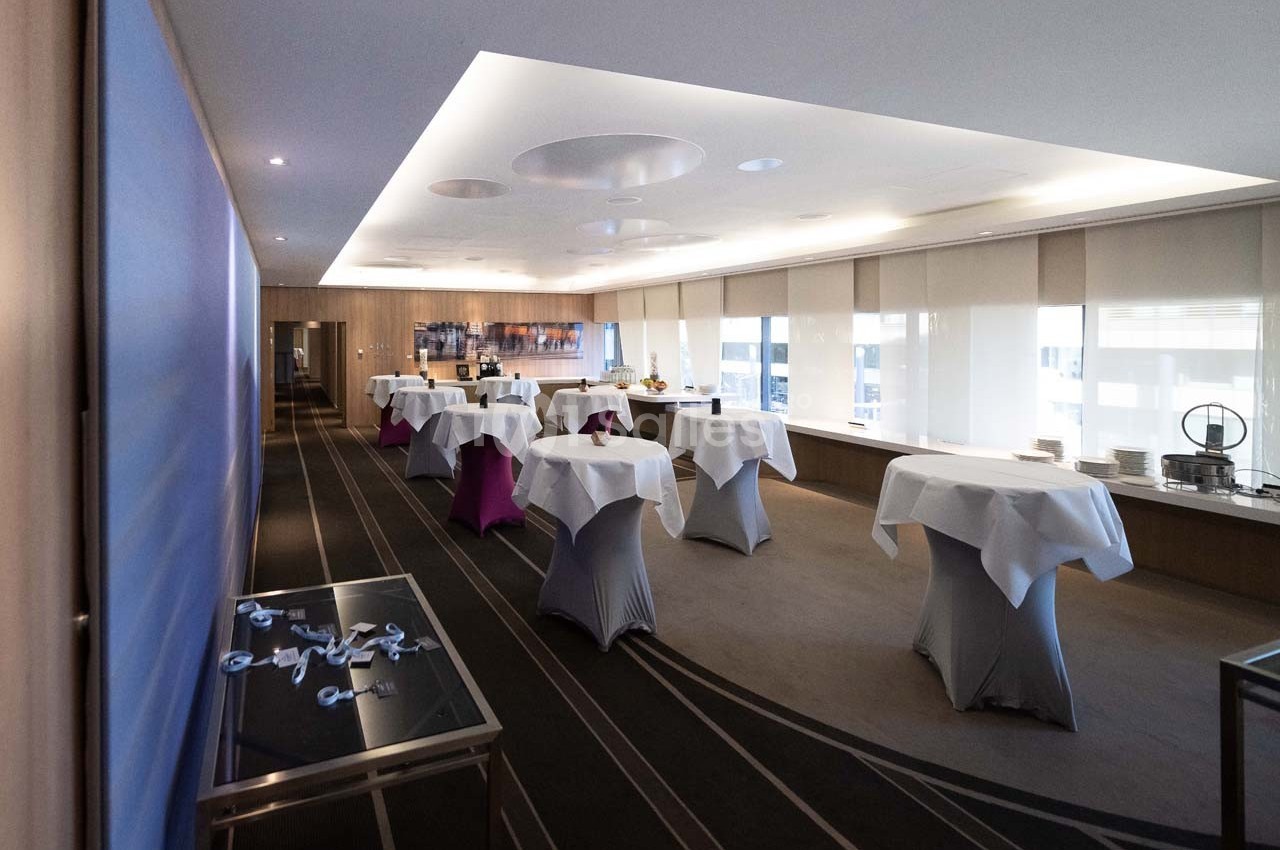 Salle de réception lumineuse avec des tables recouvertes de nappes blanches, prête pour un événement.