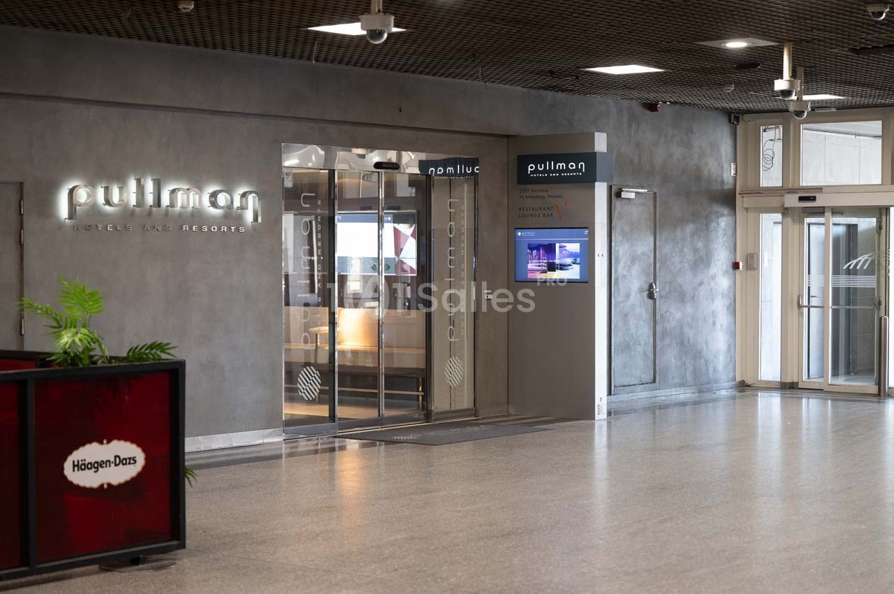 Entrée d'un hôtel Pullman avec portes vitrées, enseigne lumineuse et un écran d'information à droite.