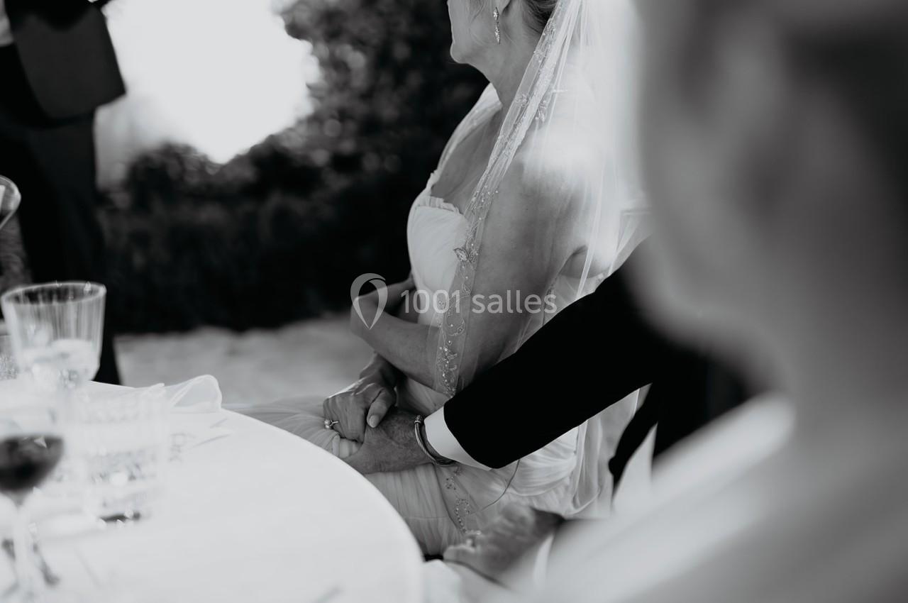 Un couple assis, la mariée en robe blanche et voile, tenant la main de son partenaire lors d'une réception.