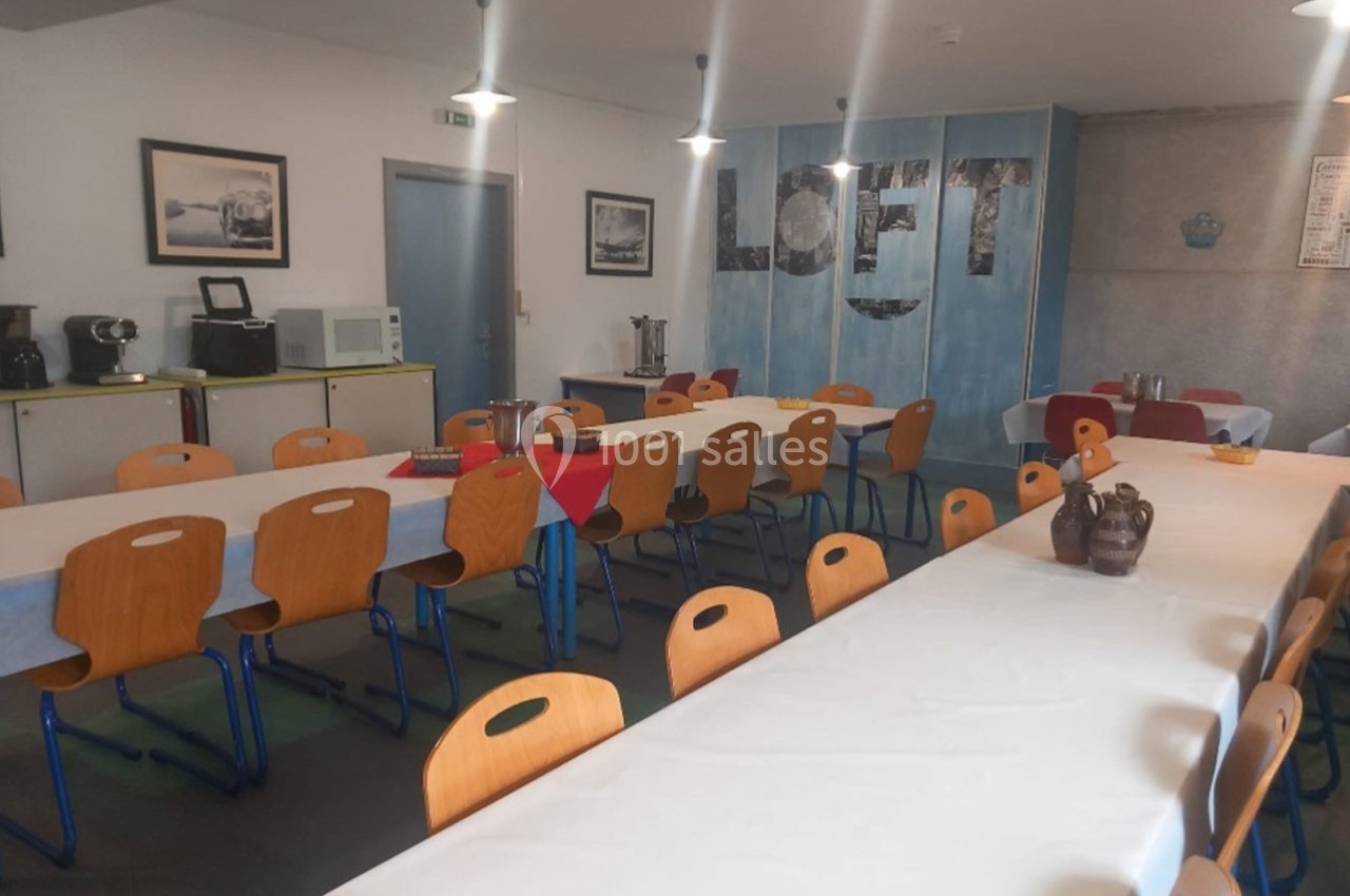 Salle à manger avec longues tables couvertes de nappes blanches, chaises en bois et décorations murales.