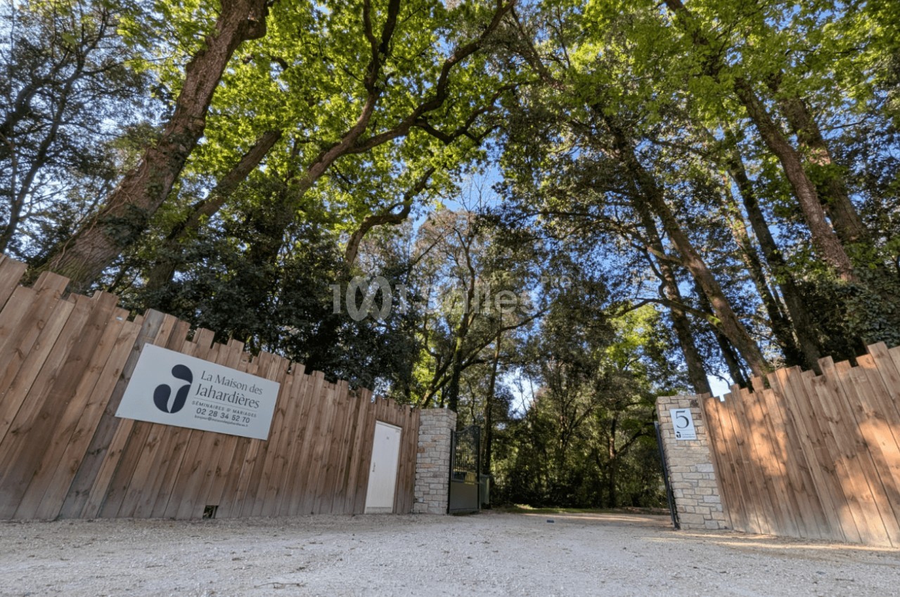 Entrée d'un domaine entouré d'arbres, avec une clôture en bois, un panneau et un portail ouvert.