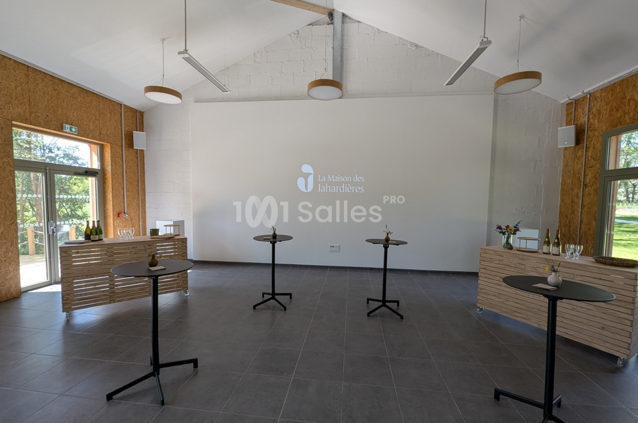 Salle lumineuse avec tables hautes, murs blancs, parquet gris et logo ’La Maison des Lahardières’ projeté au mur.