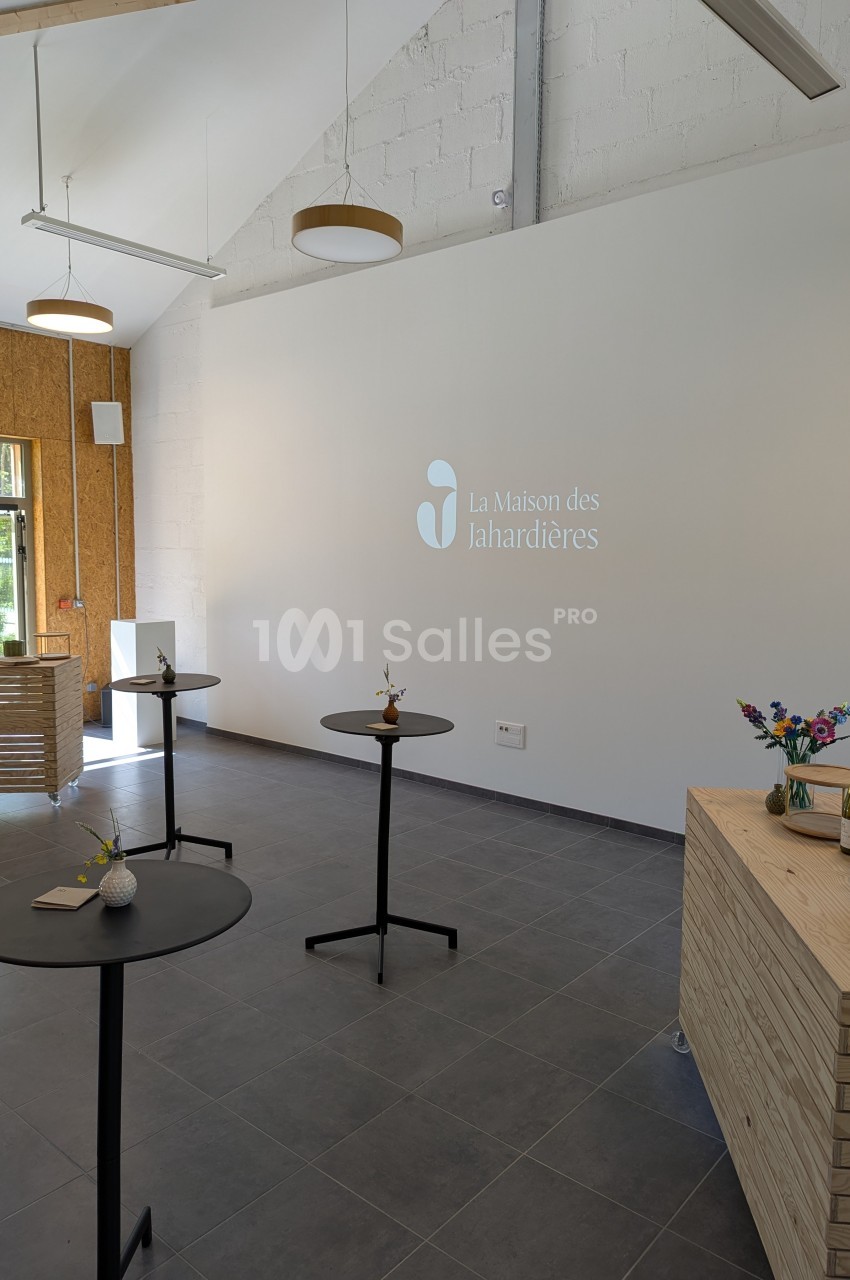 Salle lumineuse avec tables hautes, décor minimaliste, logo ’La Maison des Lahardières’ projeté sur un mur blanc.
