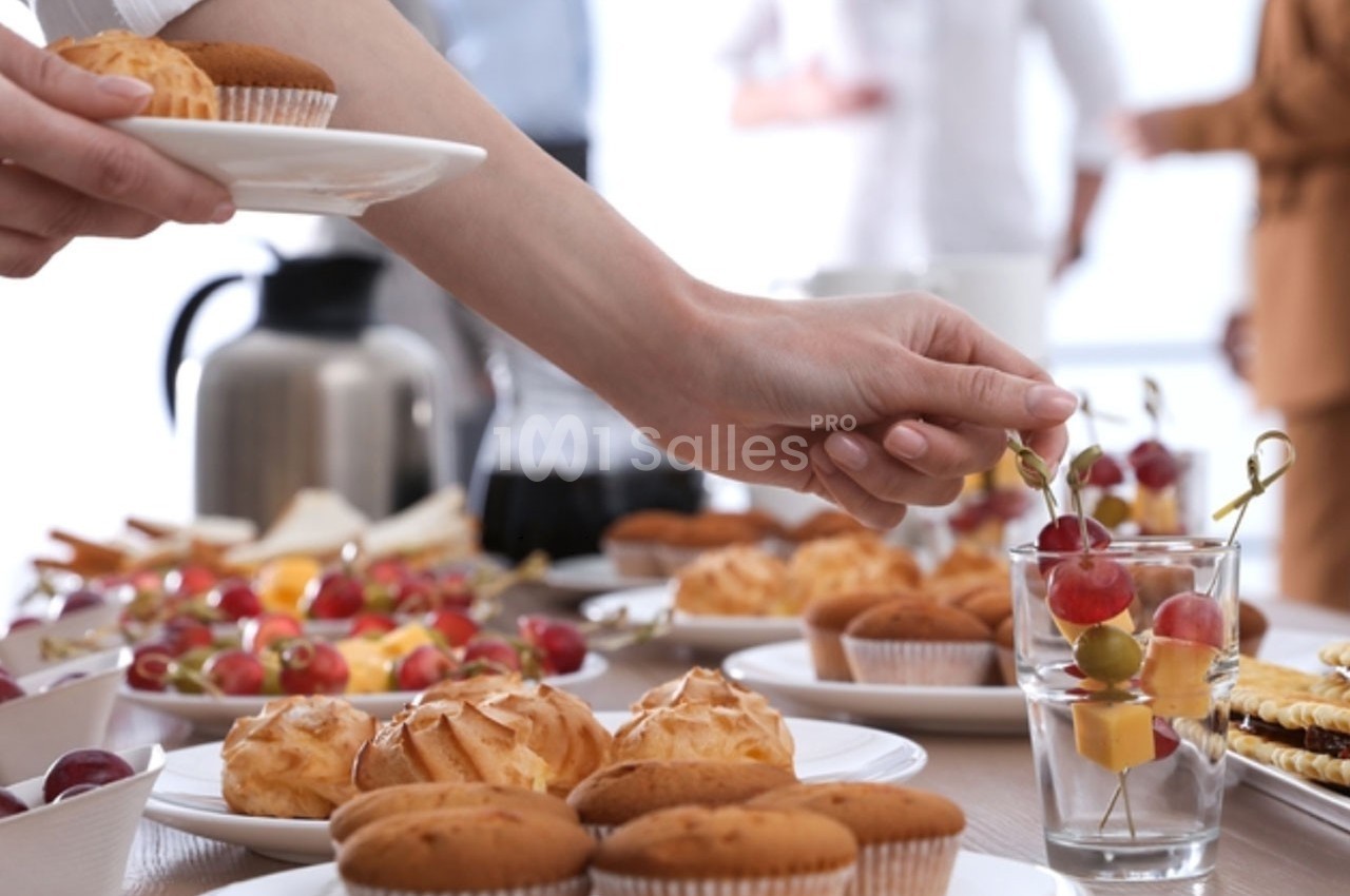 Personne prenant une brochette de fruits sur une table garnie de pâtisseries et d'autres aliments.
