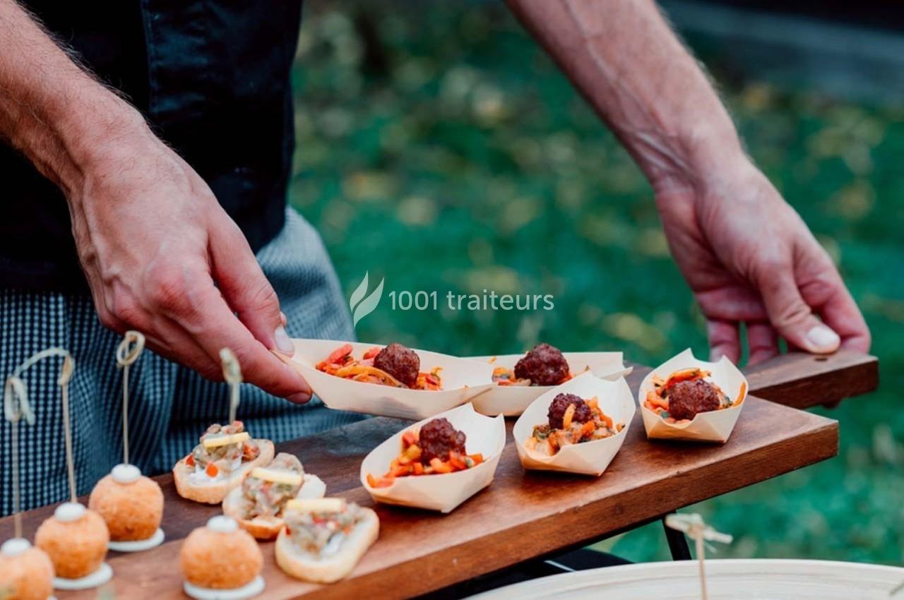 Un serveur présente des amuse-bouches dans des barquettes en bois, composés de boulettes de viande et de garnitures colorées.