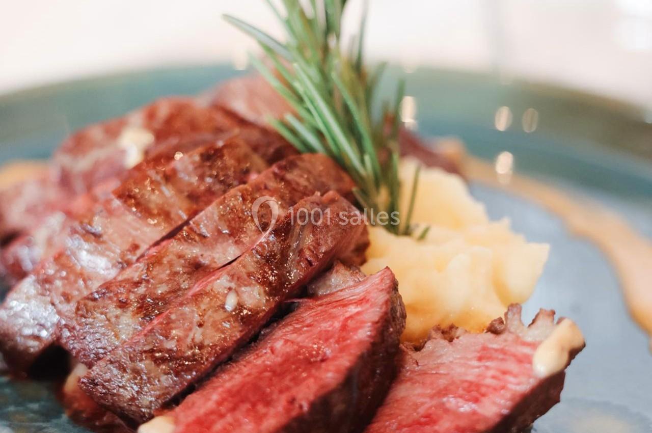 Tranches de steak saignant servies sur une purée de pommes de terre, décorées d'une branche de romarin.