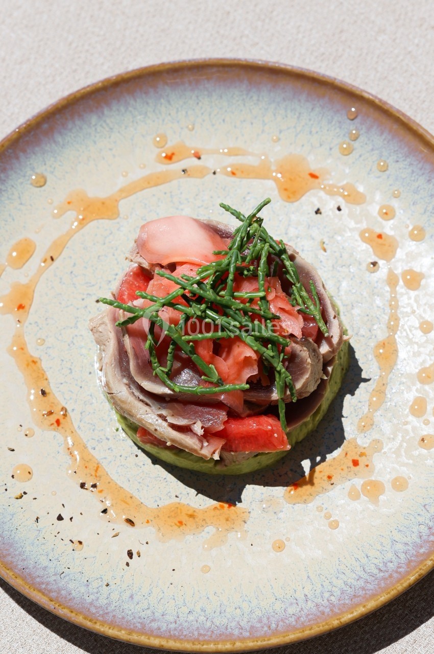 Assiette contenant une entrée composée de poisson, légumes frais, herbes et sauce, présentée sur une table claire.