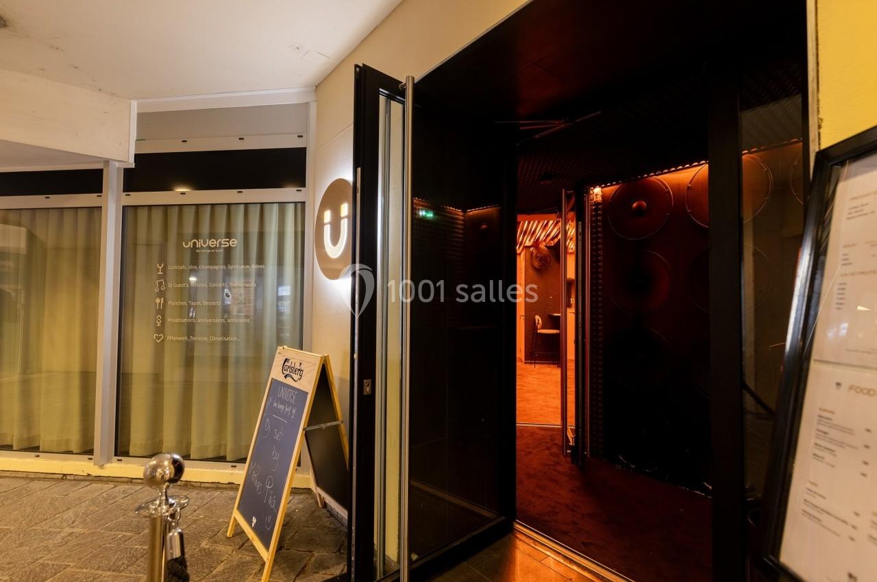 Entrée d'un établissement avec porte ouverte, intérieur éclairé en orange et panneau d'affichage à l'extérieur.