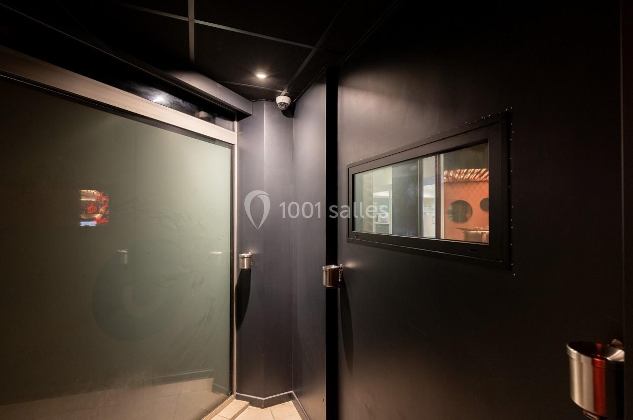 Porte vitrée et mur noir avec une fenêtre intérieure donnant sur une pièce éclairée.