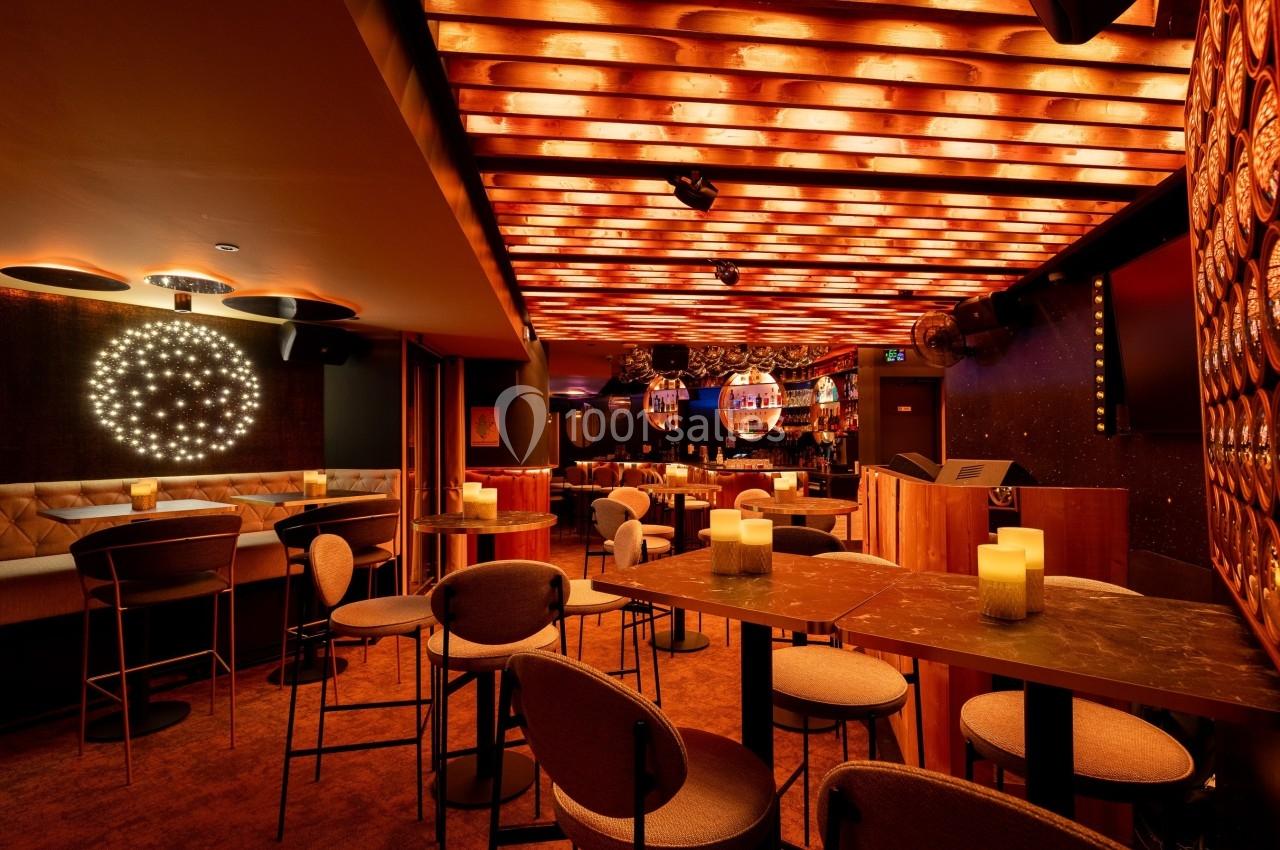 Salle de bar avec éclairage chaleureux, tables hautes, chaises modernes et décorations lumineuses au plafond.