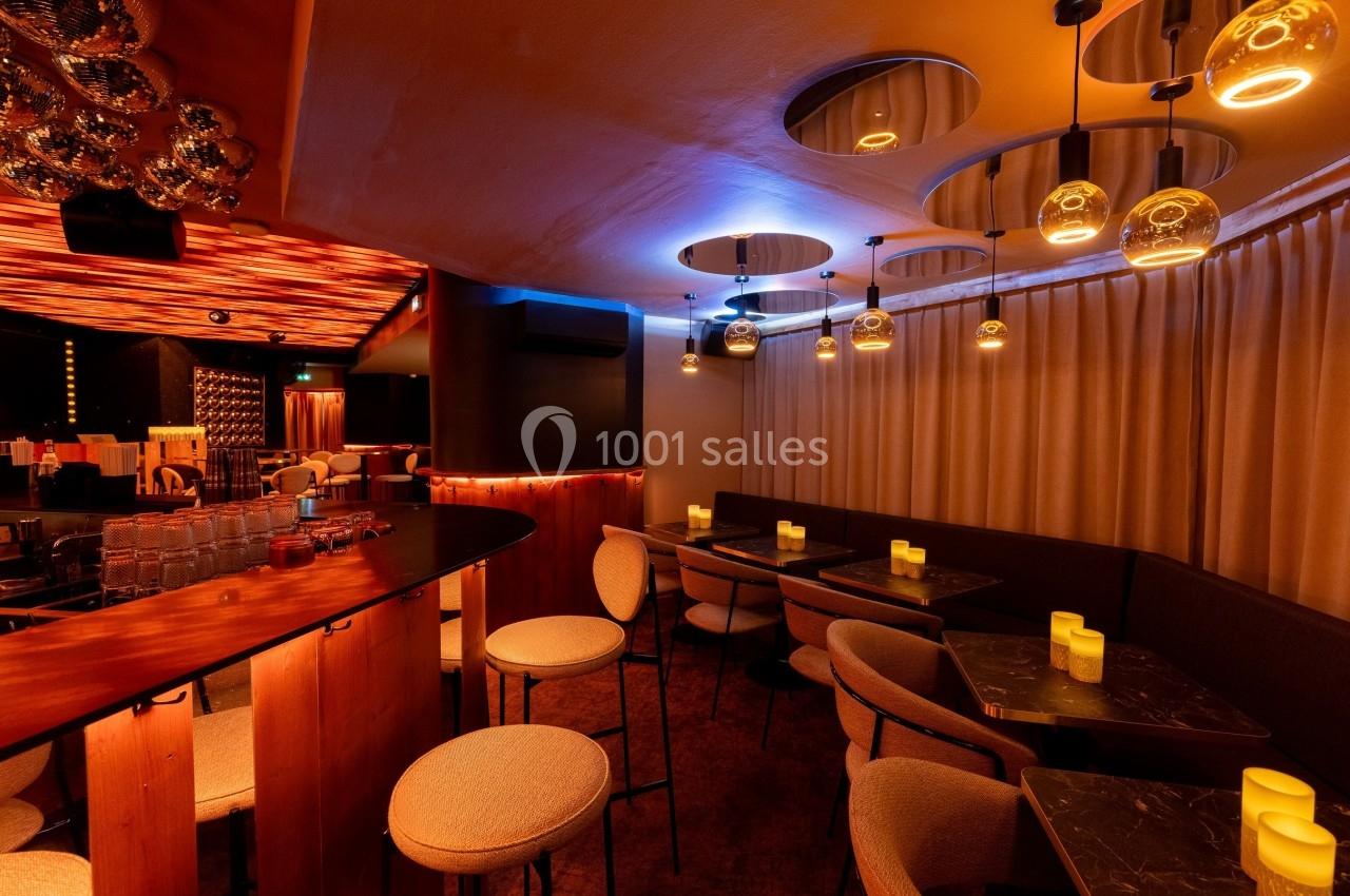 Salle de bar moderne avec éclairage tamisé, tables en marbre noir, chaises rembourrées et rideaux beiges.