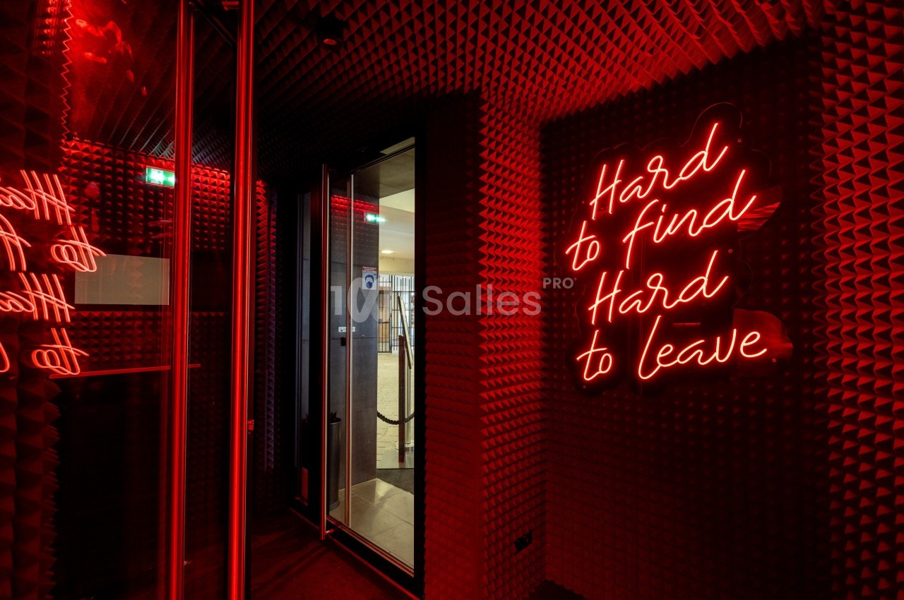 Mur recouvert de panneaux acoustiques rouges avec une enseigne néon indiquant ’Hard to find, Hard to leave’.