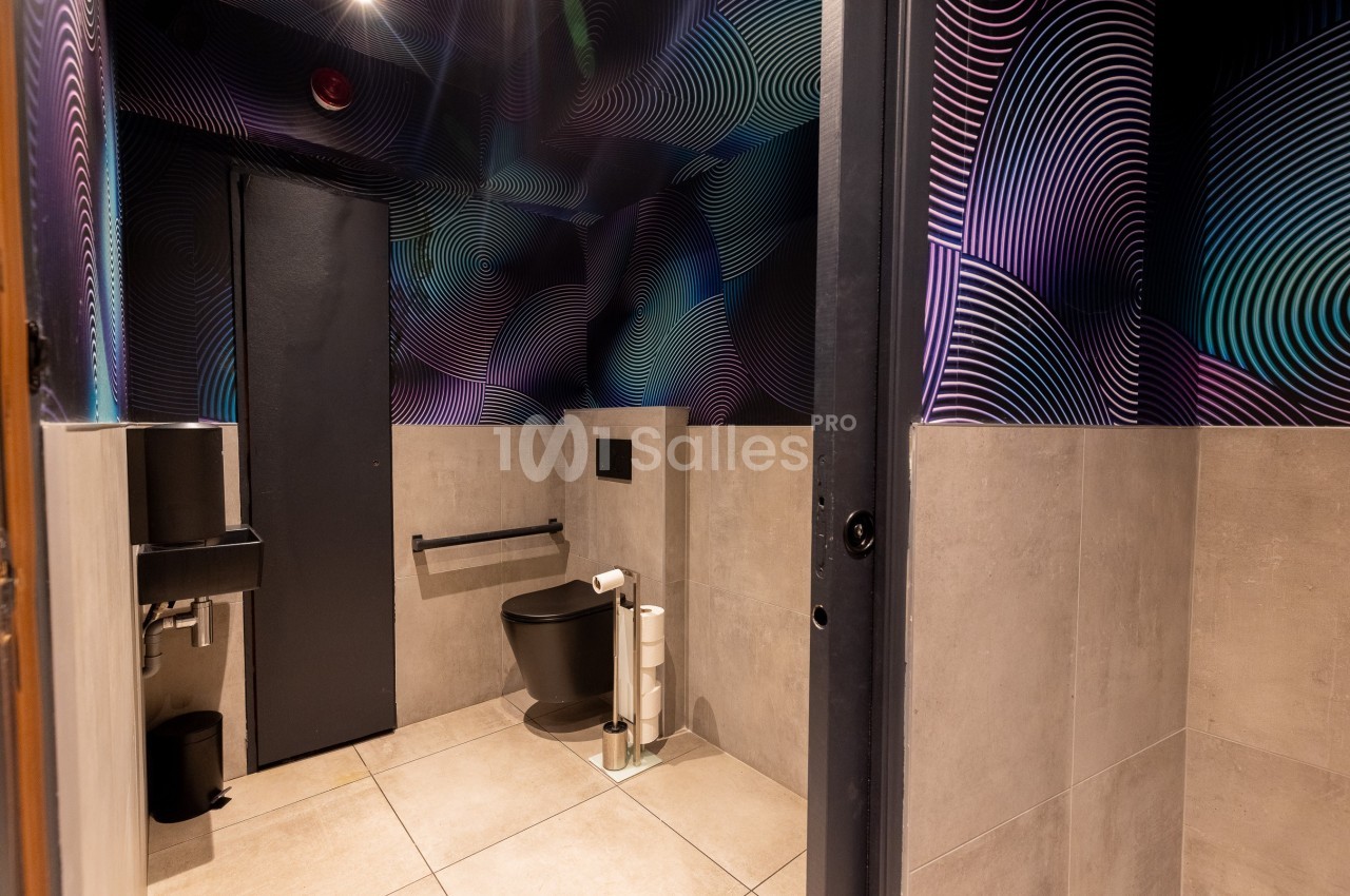 Toilettes modernes avec murs décorés de motifs géométriques colorés, sol en carrelage beige et équipements noirs.