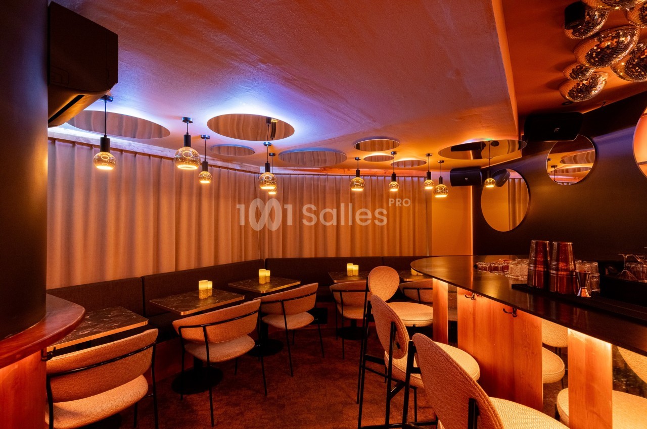 Salle de restaurant avec éclairage tamisé, tables en bois, chaises rembourrées et rideaux beige en arrière-plan.