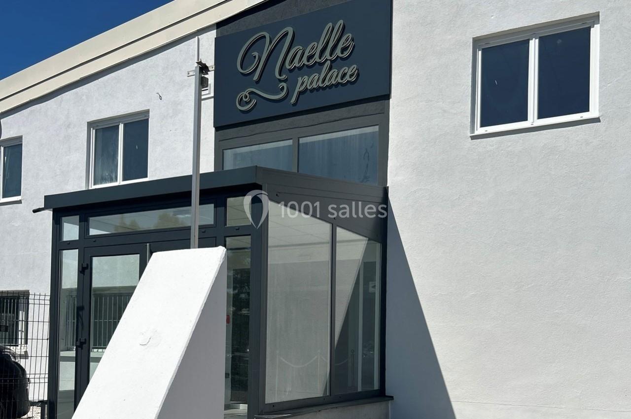 Façade d'un bâtiment blanc avec une entrée vitrée et une enseigne ’Naelle Palace’ visible au-dessus.