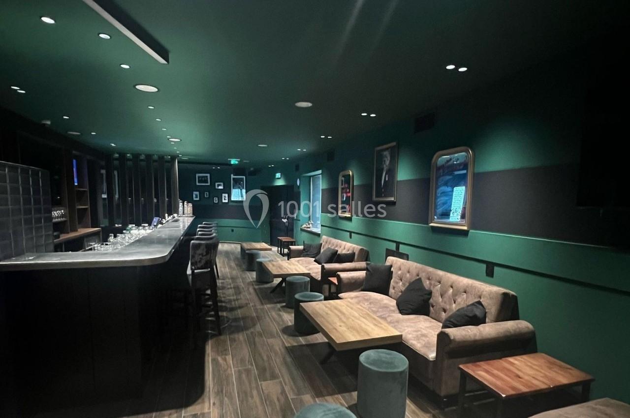Bar moderne avec comptoir long, canapés confortables, tabourets et éclairage tamisé dans une ambiance élégante.