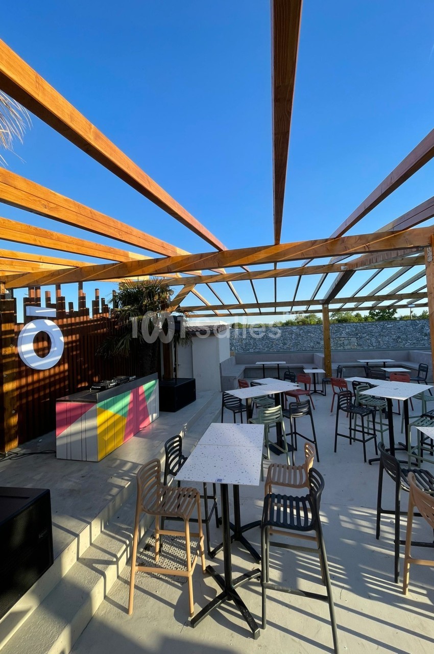 Terrasse extérieure avec tables, chaises et pergola en bois, sous un ciel bleu dégagé.