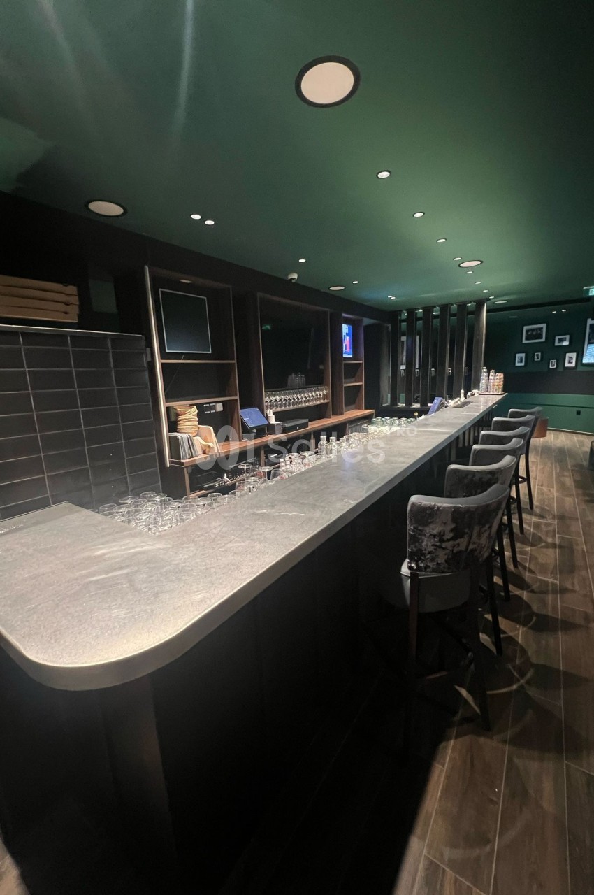 Bar avec comptoir en pierre, tabourets rembourrés, étagères en bois et éclairage tamisé dans une ambiance moderne.