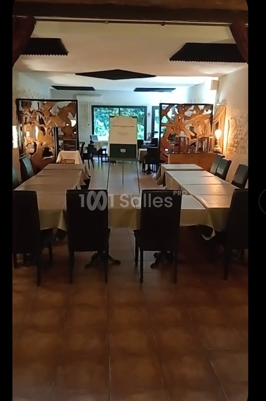 Salle de réunion avec tables rectangulaires disposées en U, chaises noires et décorations murales en bois ajouré.
