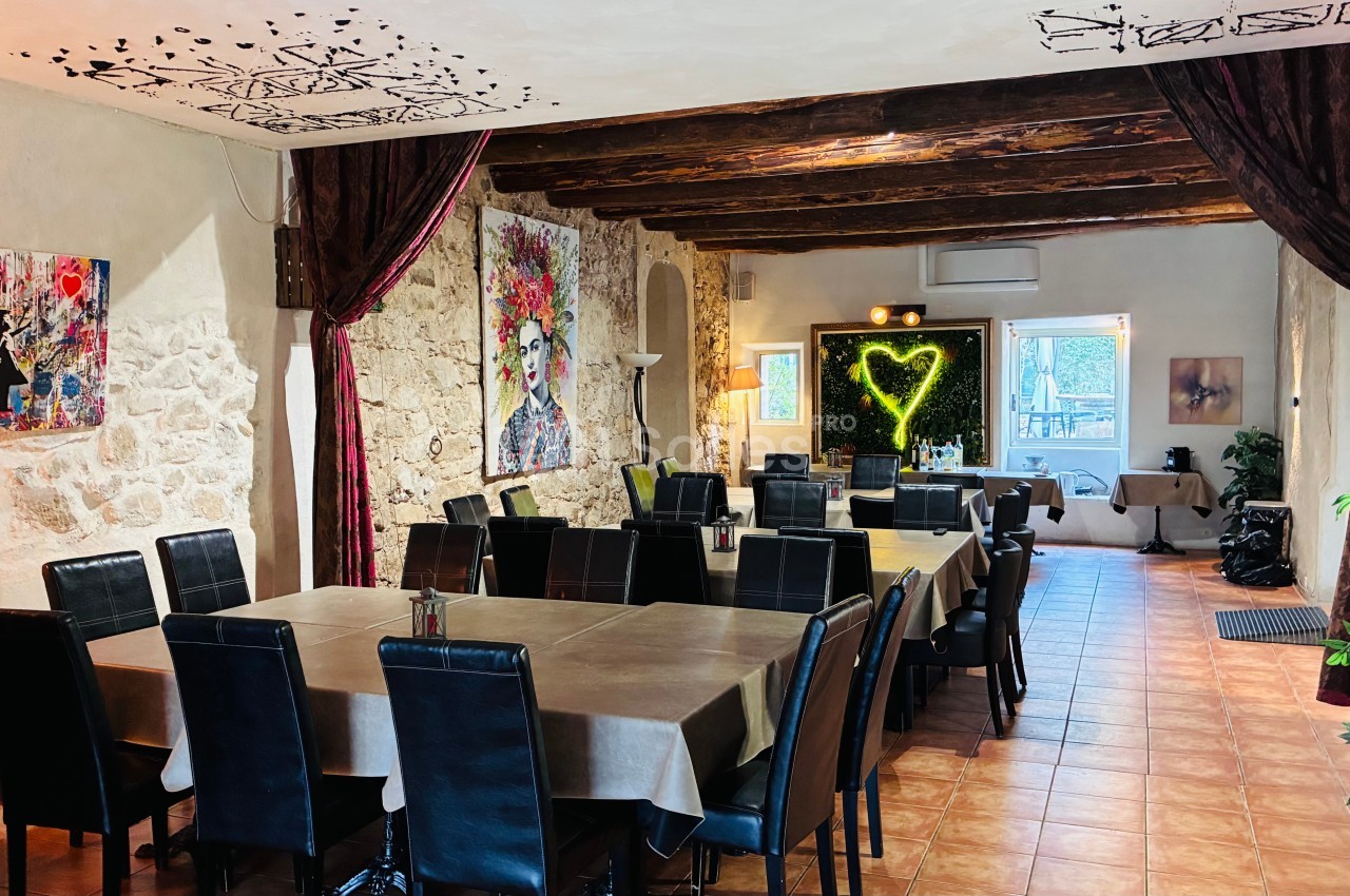 Salle de restaurant avec murs en pierre, poutres apparentes, tableaux colorés et décoration lumineuse en forme de cœur.