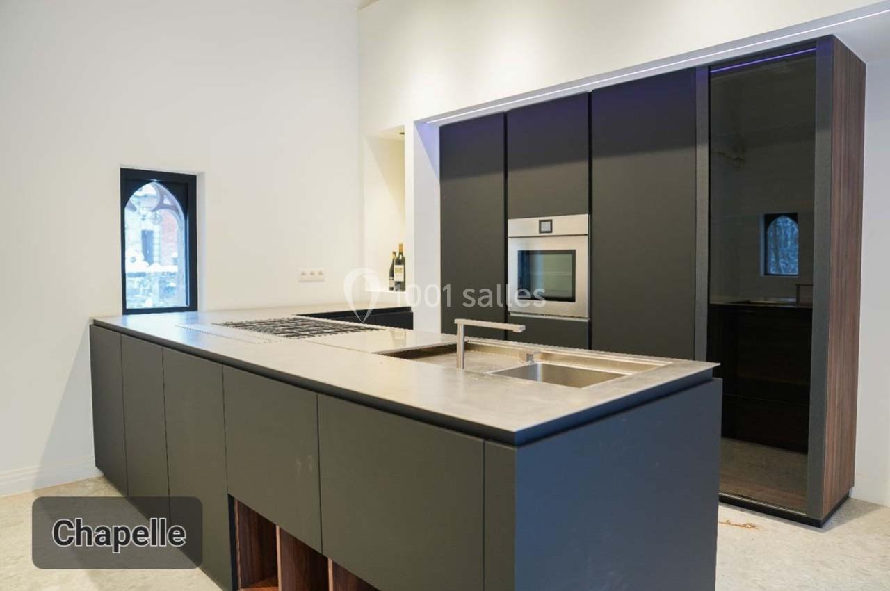 Cuisine moderne avec îlot central, évier intégré, four encastré et fenêtre en arche laissant entrer la lumière.