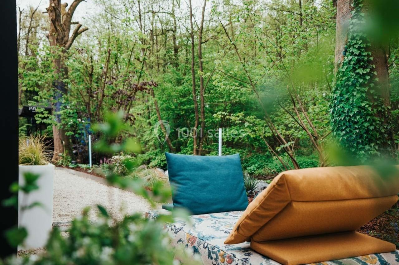 Coussins colorés disposés sur un banc dans un jardin verdoyant entouré d'arbres et de plantes.
