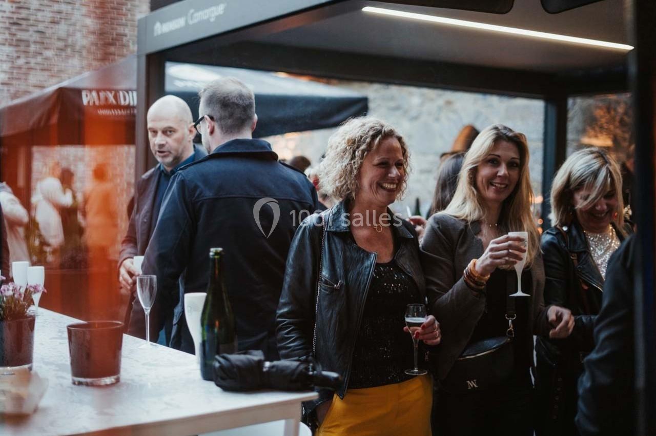Des personnes discutent et boivent des verres lors d'un événement convivial en extérieur, près d'un comptoir.