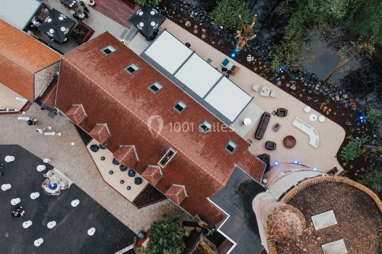 Vue aérienne d'un bâtiment en briques rouges avec une cour aménagée et un espace extérieur près d'un plan d'eau.