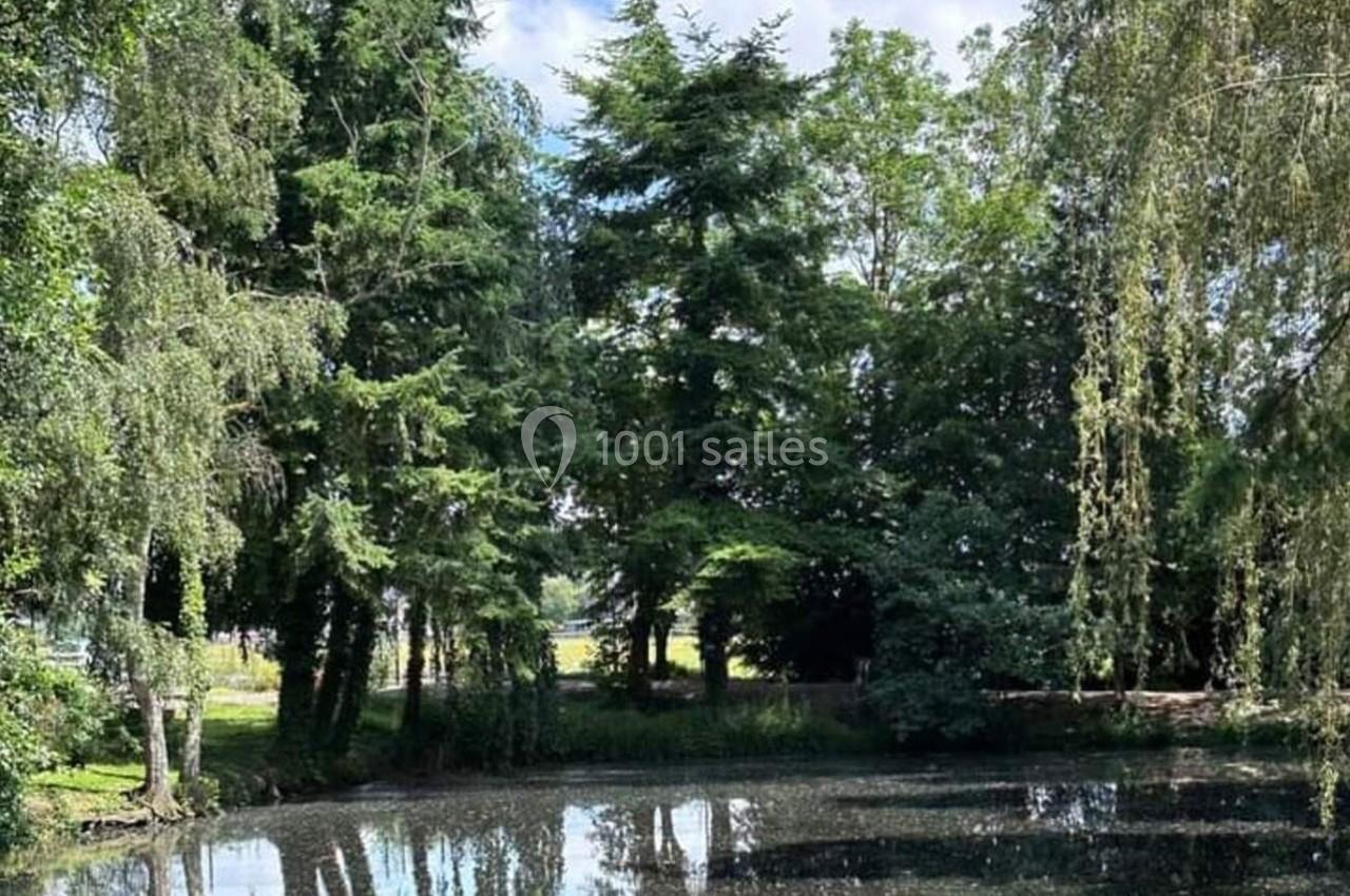 Étang entouré d'arbres et de végétation, reflétant le ciel partiellement nuageux.