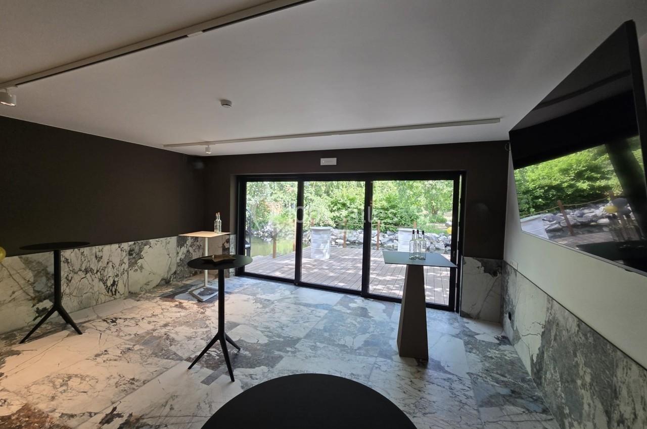 Salle lumineuse avec sol en marbre, murs sombres, tables hautes et grande baie vitrée donnant sur un espace extérieur…