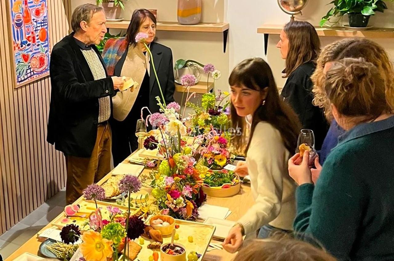 Des personnes discutent autour d'une table joliment décorée avec des fleurs et des plats variés dans un cadre convivial.