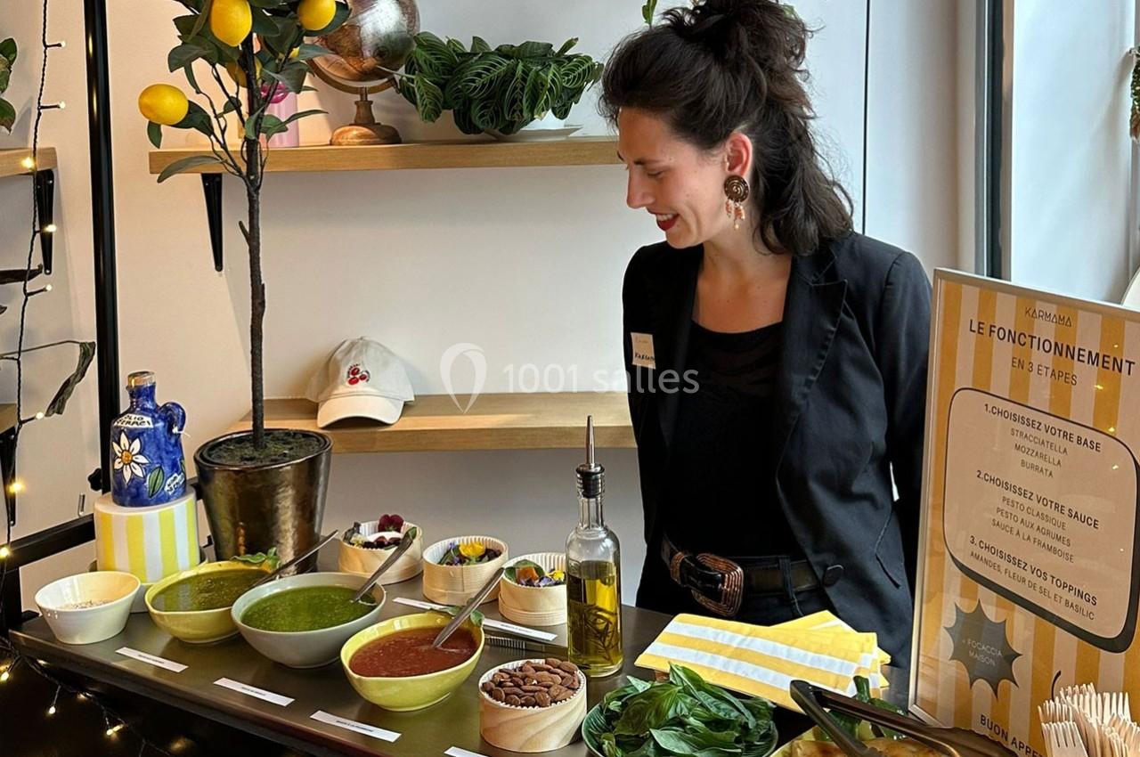 Une femme souriante se tient derrière un comptoir présentant des ingrédients variés pour préparer un plat personnalisé.